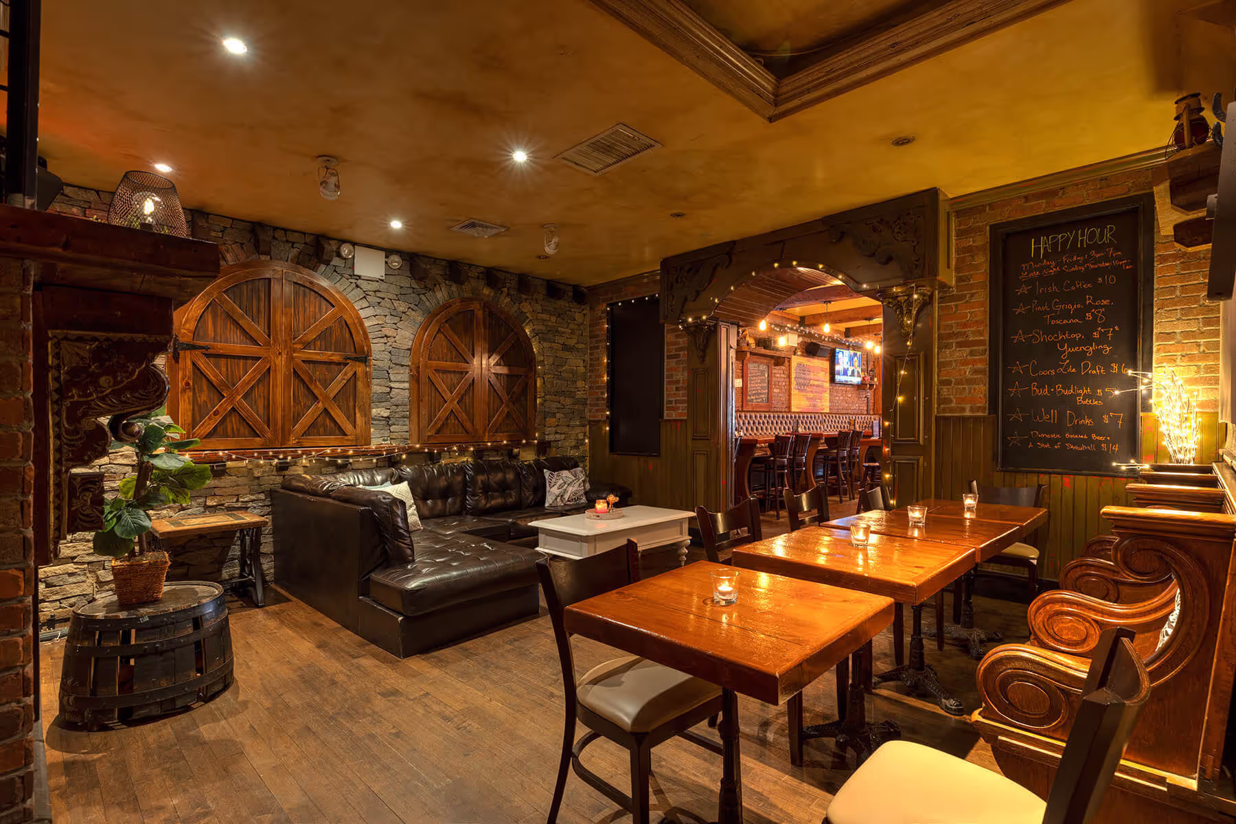 Cozy pub interior with wooden tables, leather sofa, stone walls, warm lighting, and a chalkboard displaying happy hour specials.