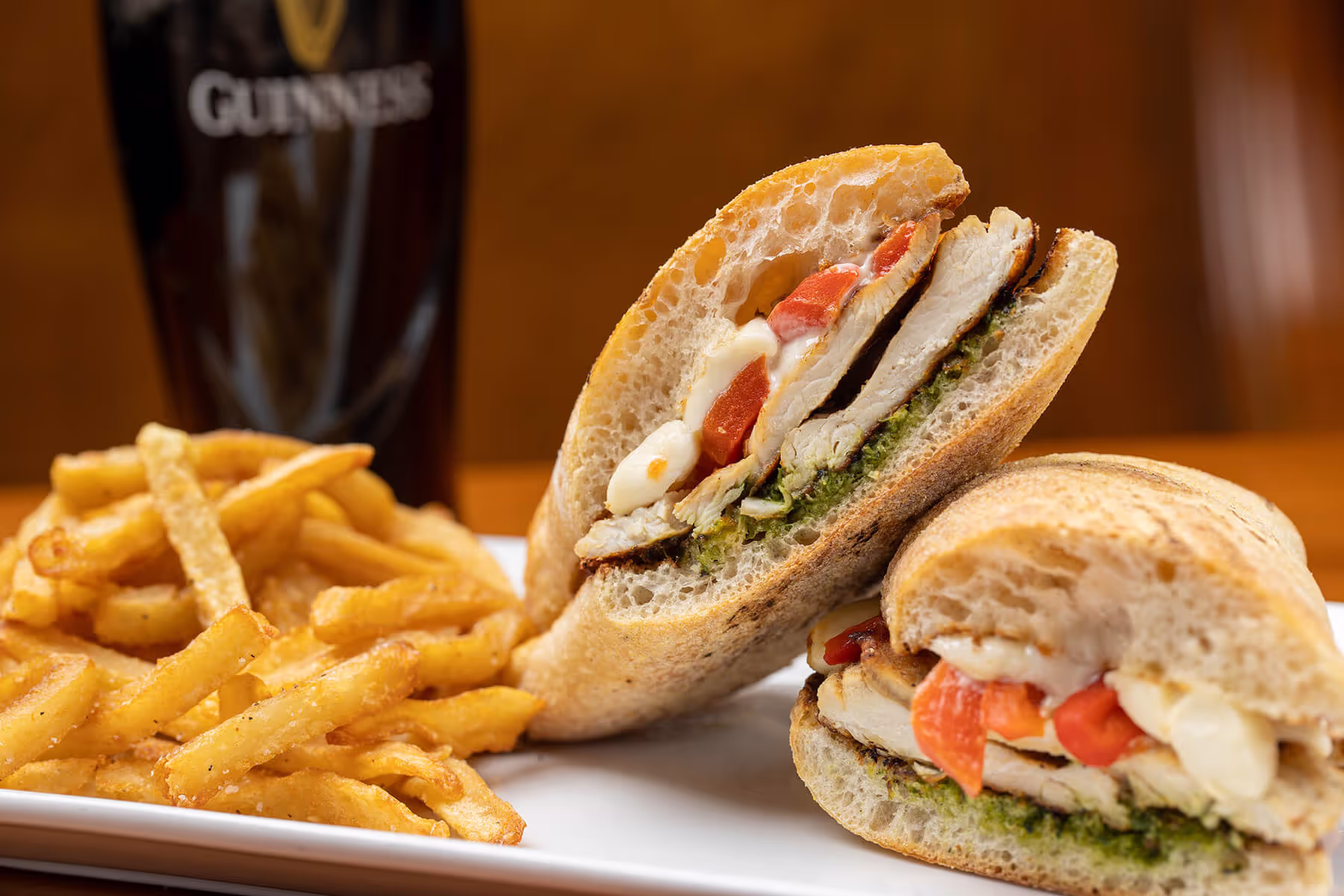 Grilled chicken sandwich with pesto, melted cheese, and roasted red peppers served with seasoned French fries and a glass of Guinness.