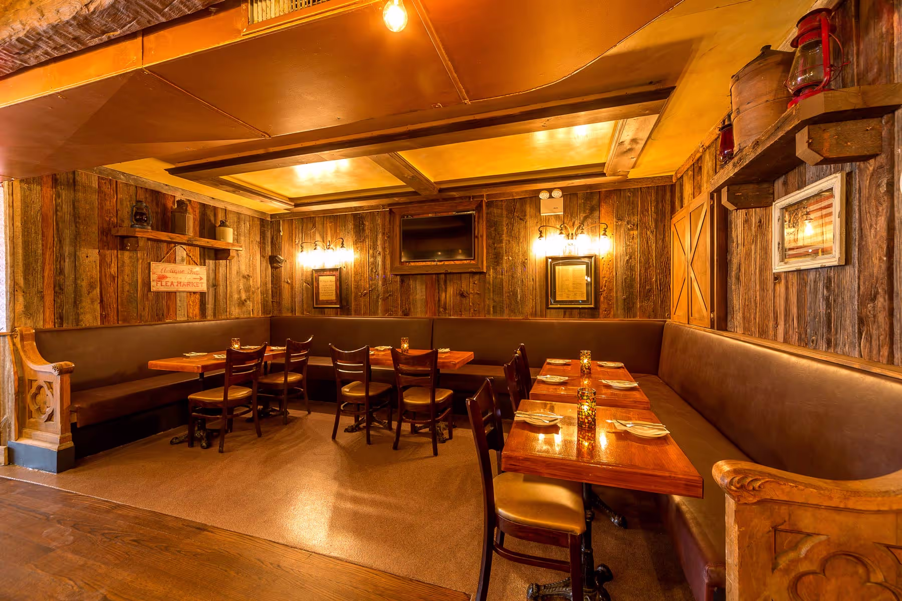 Cozy restaurant dining area with wooden walls, brown leather banquette seating, wooden tables set with napkins and cutlery, and warm lighting.